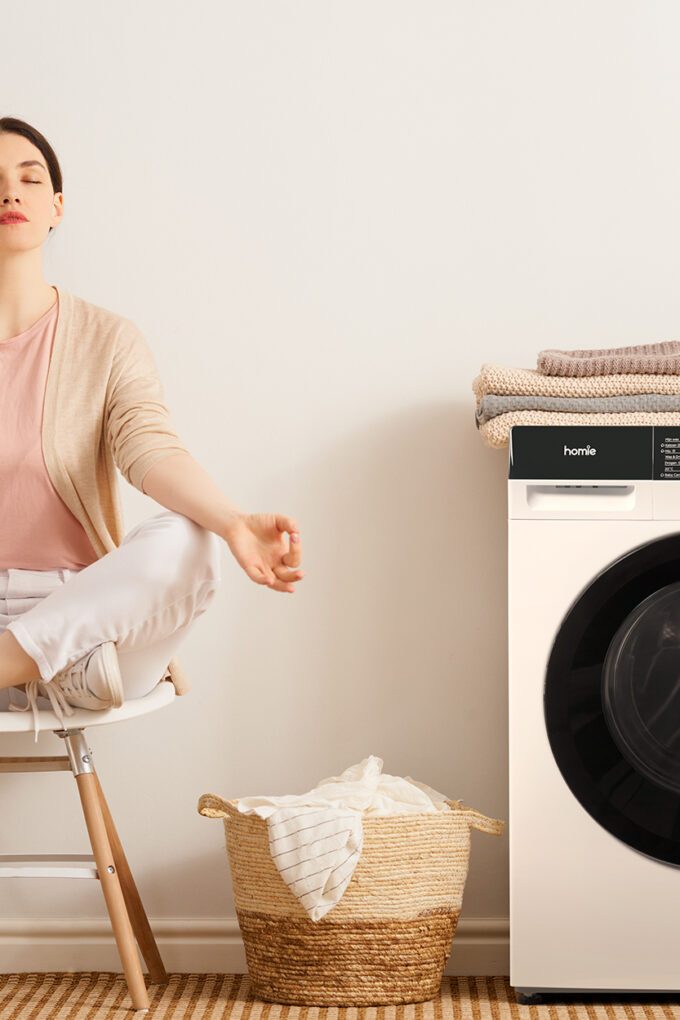 Vrouw zit te mediteren naast wasmachine omdat ze zich ontspannen voelt door een goede wasroutine